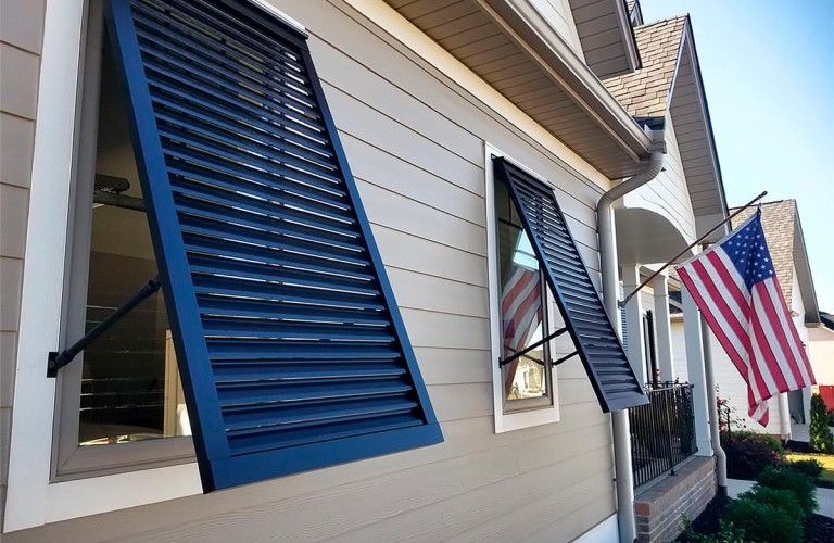 Decorative Bahama shutters partially open, providing both shade and storm protection for home windows.